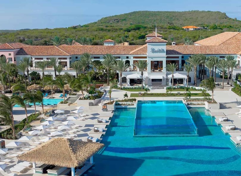 Испанийн ус, ширүүн уулын ландшафтыг харсан өргөн дээд доод тавцан бүхий Sandals Royal Curacao дахь Dos Awa Infinity Pool | eTurboNews | eTN